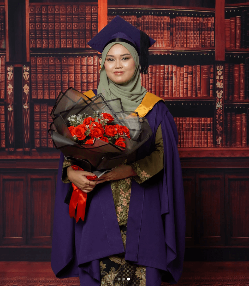 Graduan berjubah ungu pegang jambangan ros merah di Sénira Studio