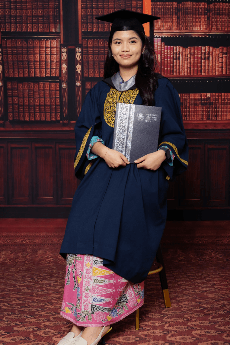 Graduan berjubah biru tua dengan kain songket merah jambu