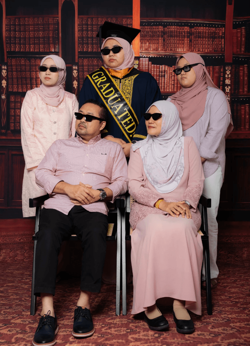 Graduan bersama keluarga, semua pakai cermin mata hitam, di Sénira Studio